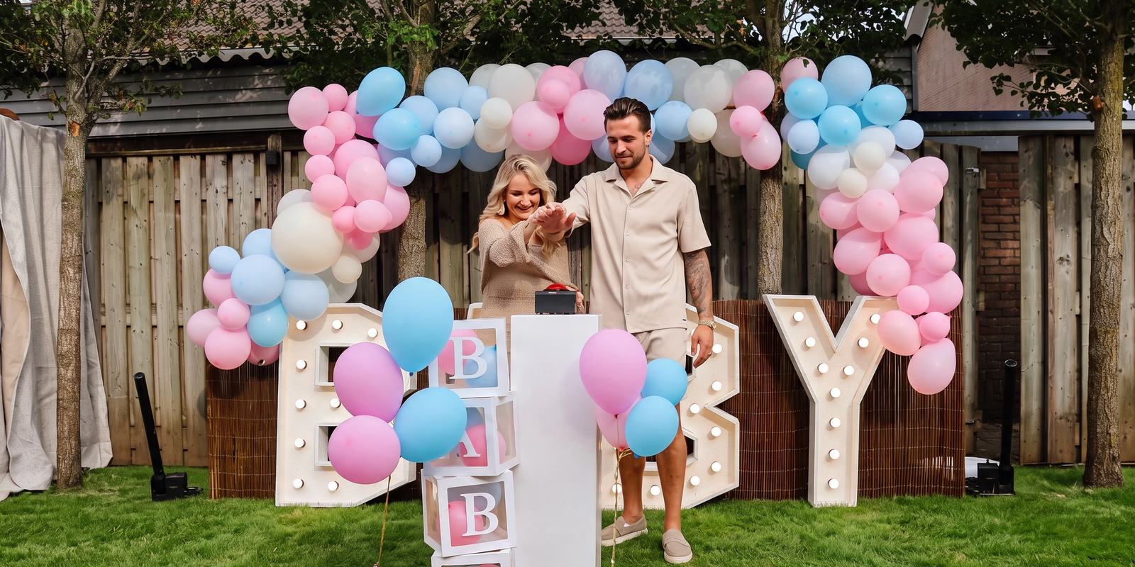 Gender reveal opstelling met vier statafels met roze rok, BABY-lichtletters en witte stoelen